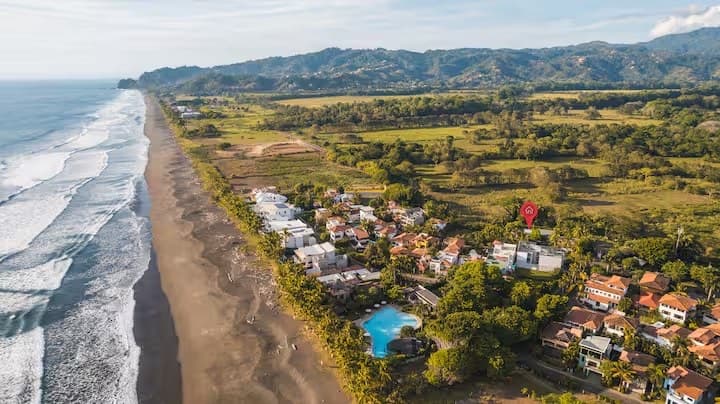 Aerial view of Playa Hermosa, a quieter stretch of coastline south of Jacó with scattered houses and vegetation.
